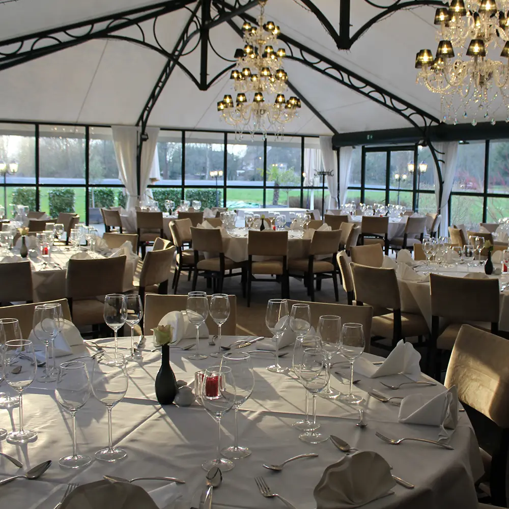 De orangerie feestelijk gedekt met kroonluchters en ronde tafels